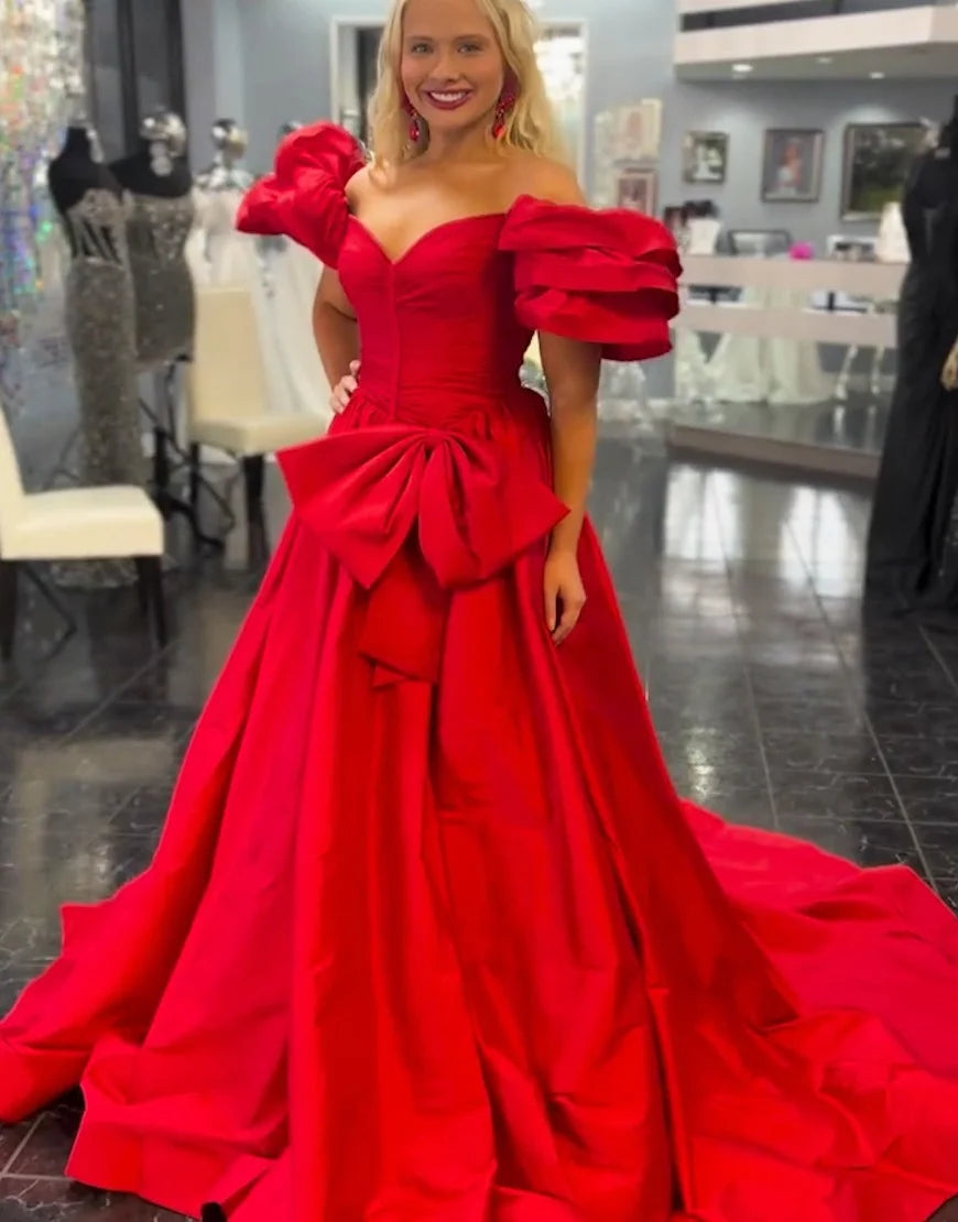 bright red off-the-shoulder ball gown with dramatic ruffled sleeves, a fitted bodice, a large bow at the waist, and a long train