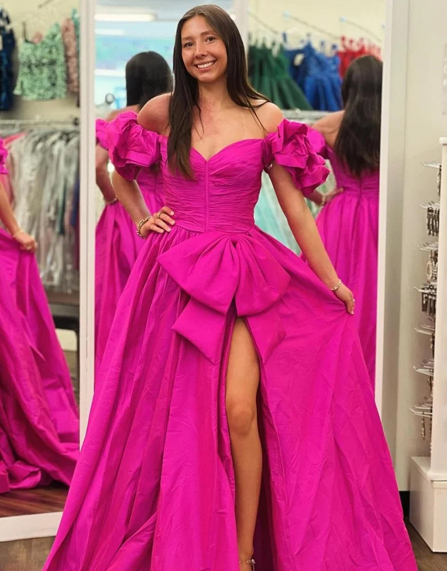 bright fuchsia pink off-the-shoulder evening gown with a sweetheart neckline, ruched bodice, large bow detail at the waist, and a high thigh slit