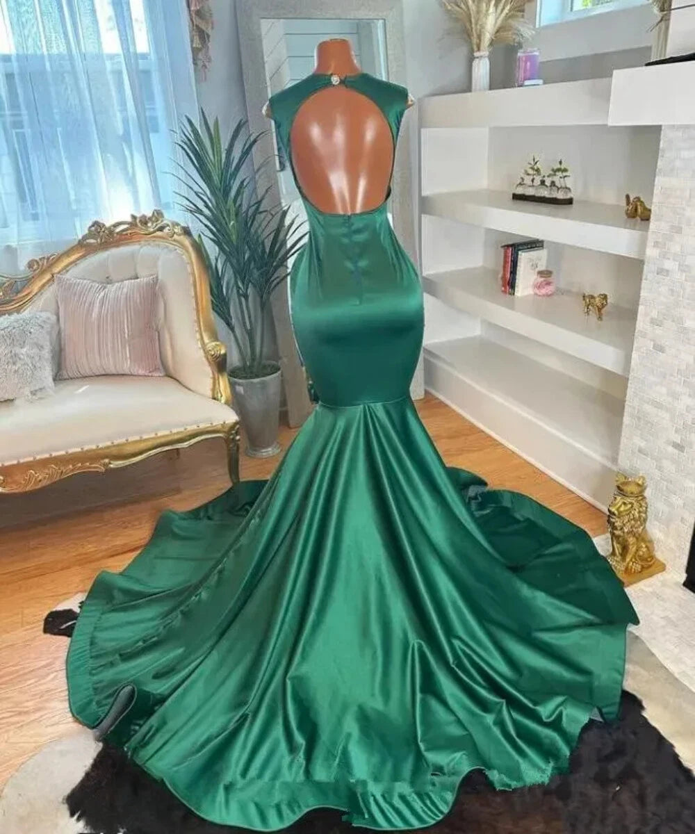A emerald green satin mermaid-style evening gown. The dress has a high open back, fitted silhouette, and a full flared skirt with a train.