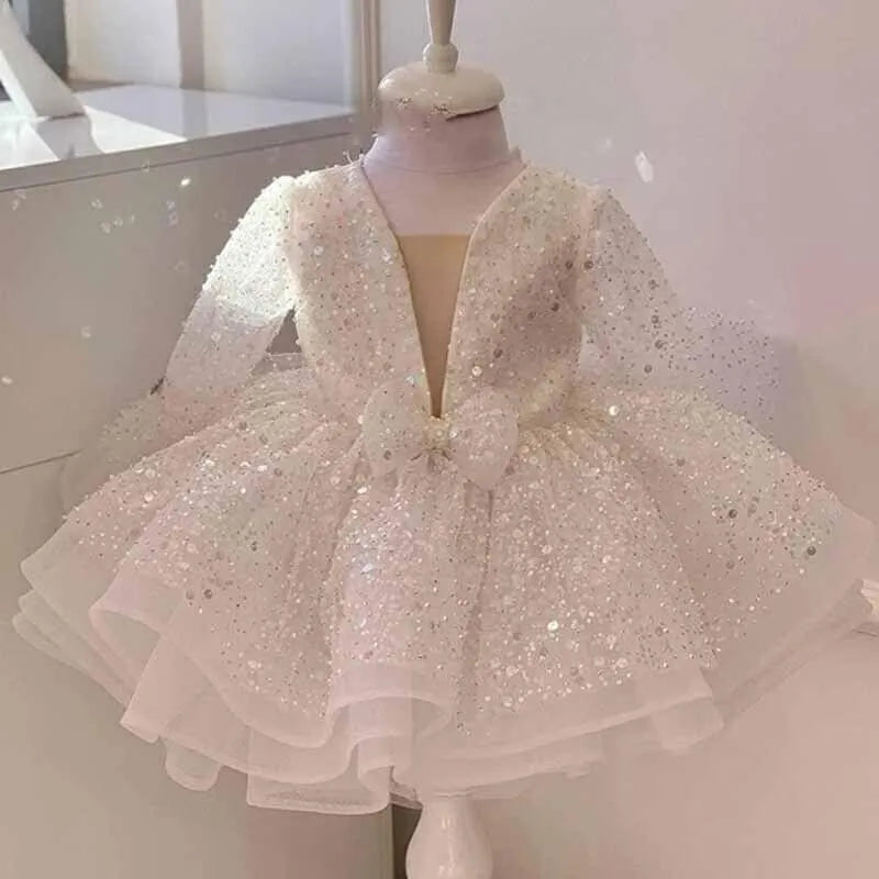 A sparkling white long-sleeve toddler party dress with a deep V-neckline, a large bow at the waist, and a layered ruffled tulle skirt