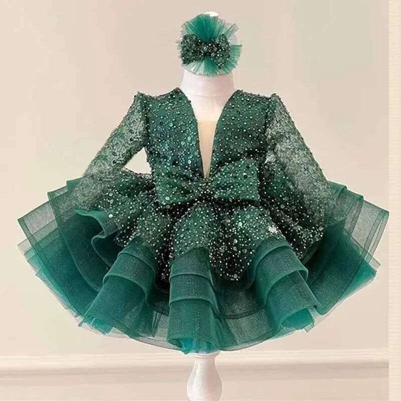 A dark green sequined and tulle formal dress , featuring long sheer sleeves, a deep V-neckline, a large bow at the waist, and a matching headpiece.